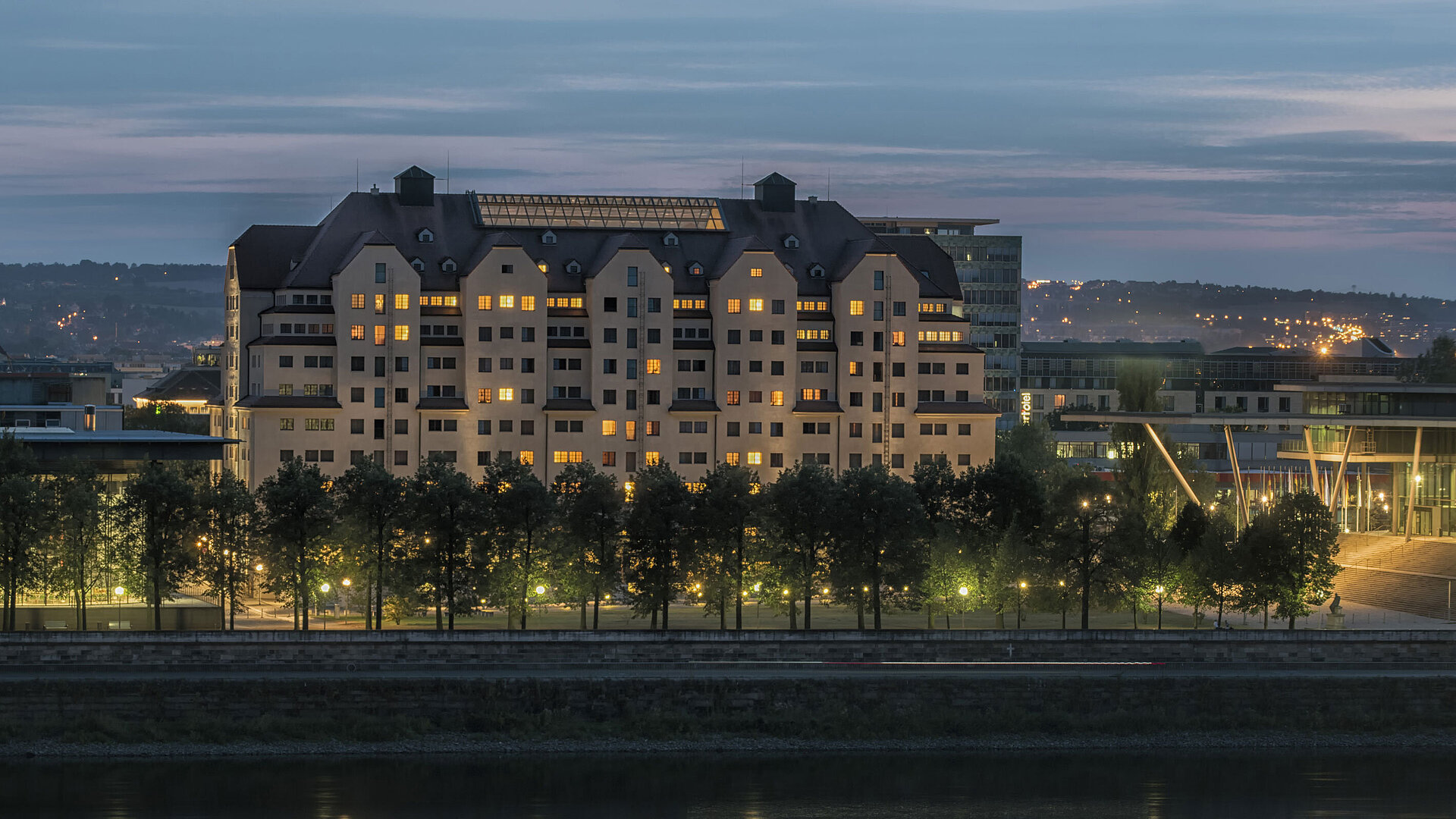 Außenansicht bei Nacht Beleuchtetes Maritim Hotel Dresden bei Dämmerung mit reflektierenden Lichtern auf der Elbe.