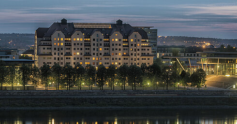 Beleuchtetes Maritim Hotel Dresden bei Dämmerung mit reflektierenden Lichtern auf der Elbe.