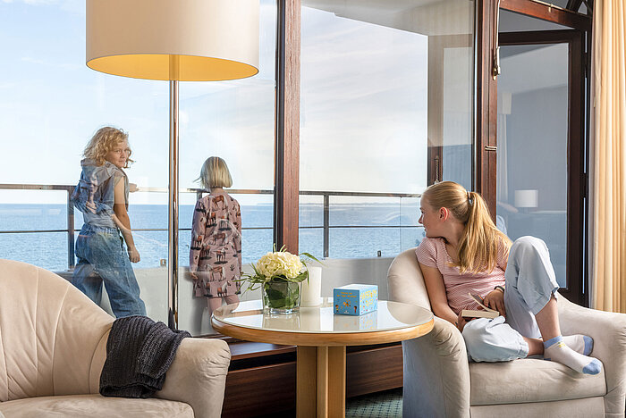 Kinder genießen den Meerblick von der Familiensuite im Maritim Hotel Timmendorfer Strand, während ein Mädchen im Sessel liest