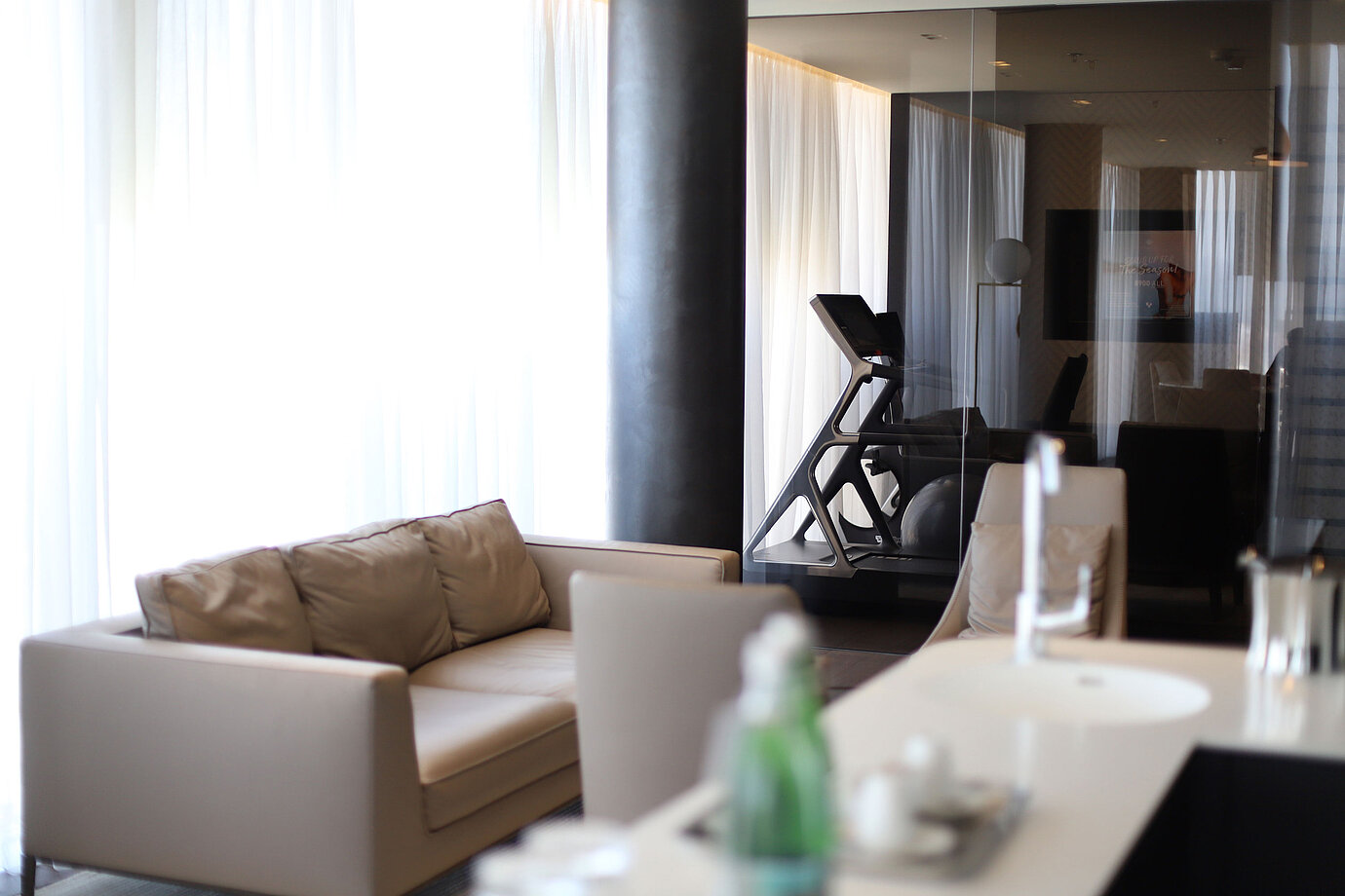Sitzecke mit Sofa und Blick auf Fitnessraum mit Laufband hinter Glas im Maritim Hotel Plaza Tirana