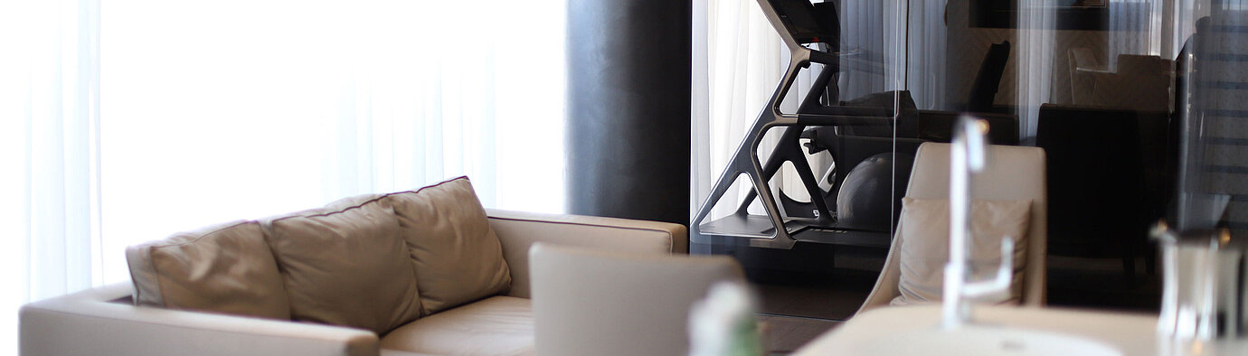 Sitzecke mit Sofa und Blick auf Fitnessraum mit Laufband hinter Glas im Maritim Hotel Plaza Tirana