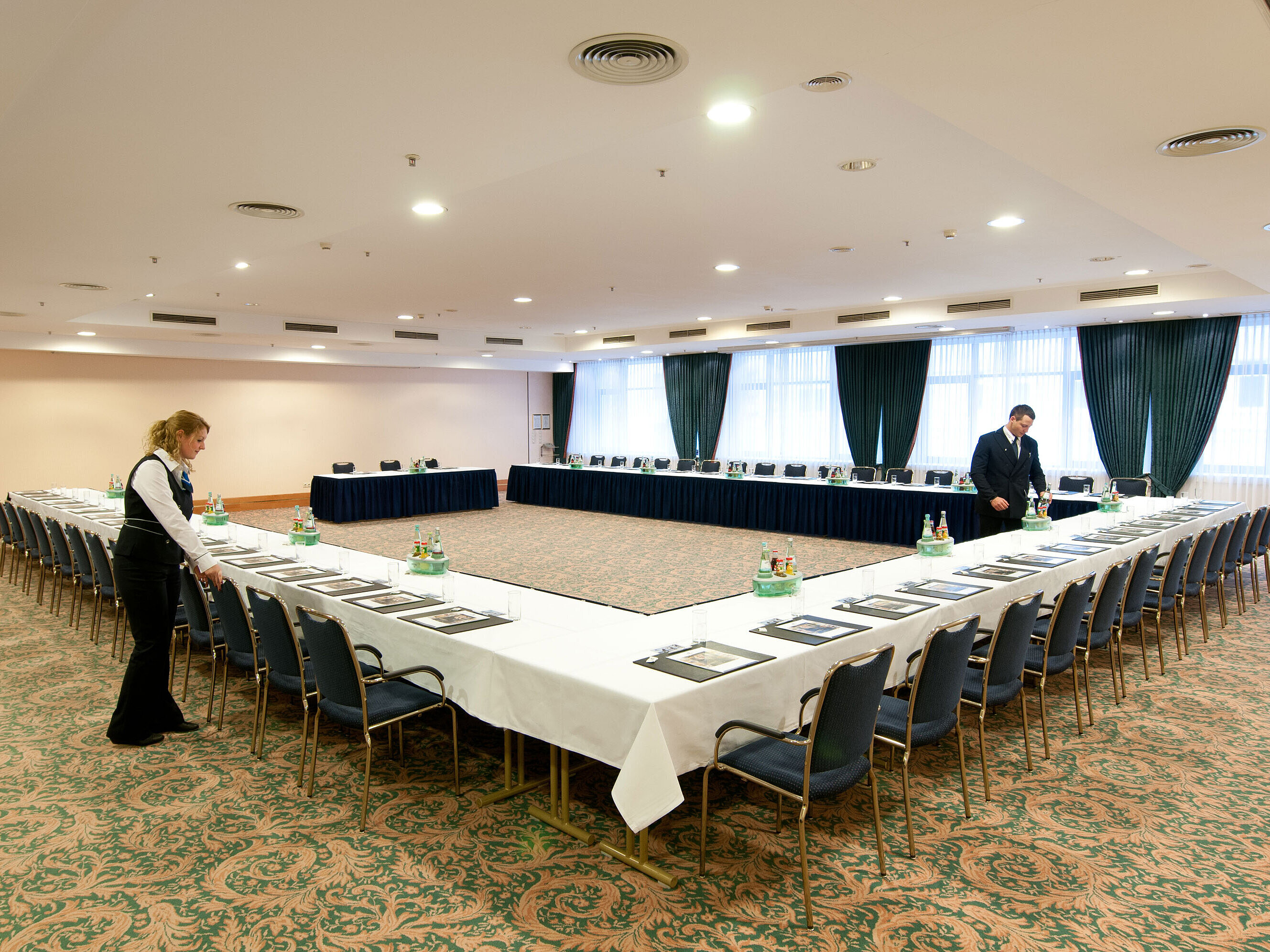 Tagungsraum Saal Berlin im Maritim Hotel Magdeburg mit U-förmiger Bestuhlung, gedeckten Tischen und Vorbereitung durch das Personal.