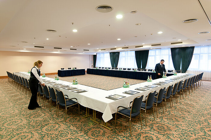 Tagungsraum Saal Berlin im Maritim Hotel Magdeburg mit U-förmiger Bestuhlung, gedeckten Tischen und Vorbereitung durch das Personal.