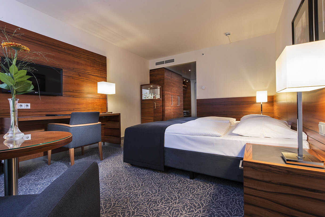 Eingerichtetes Hotelzimmer im Maritim Hotel München mit komfortablem Bett, Arbeitsbereich, TV und Holzverkleidung.