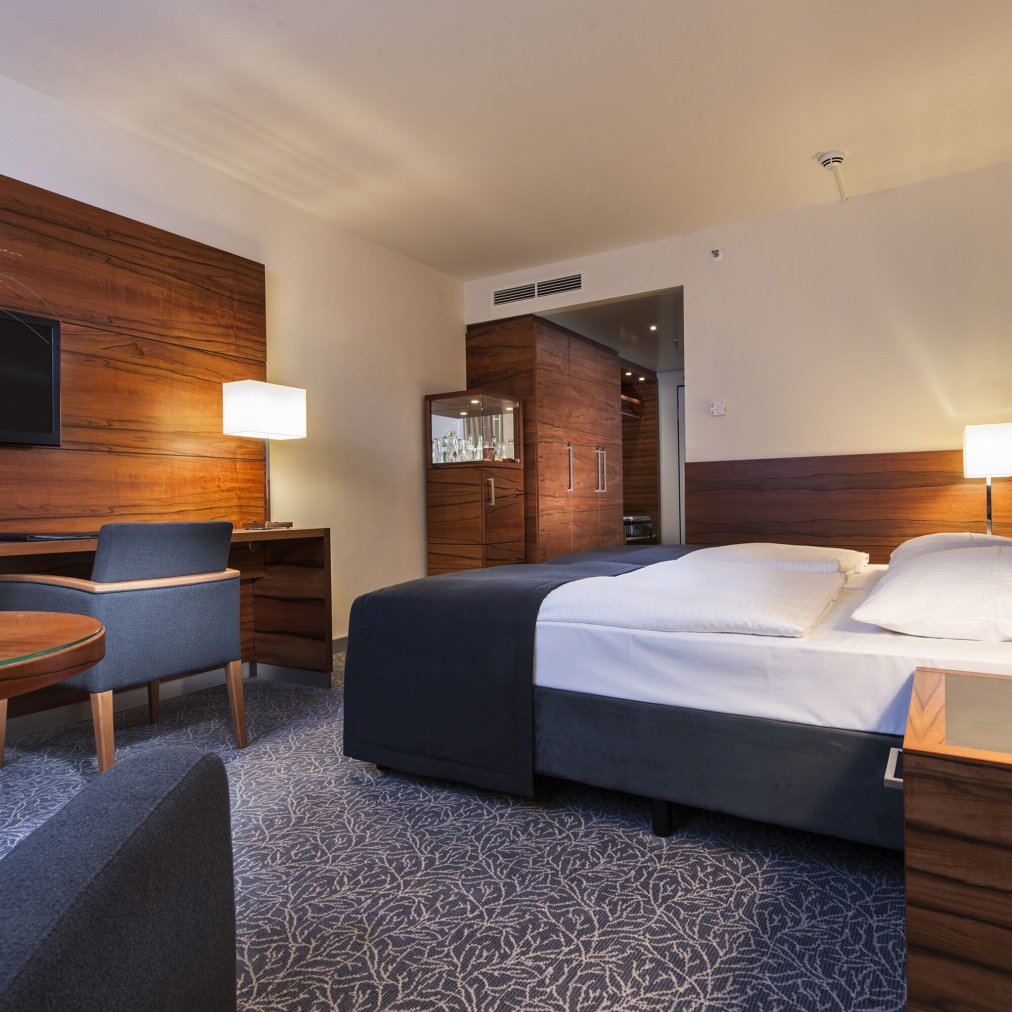 Comfort Zimmer Eingerichtetes Hotelzimmer im Maritim Hotel München mit komfortablem Bett, Arbeitsbereich, TV und Holzverkleidung.
