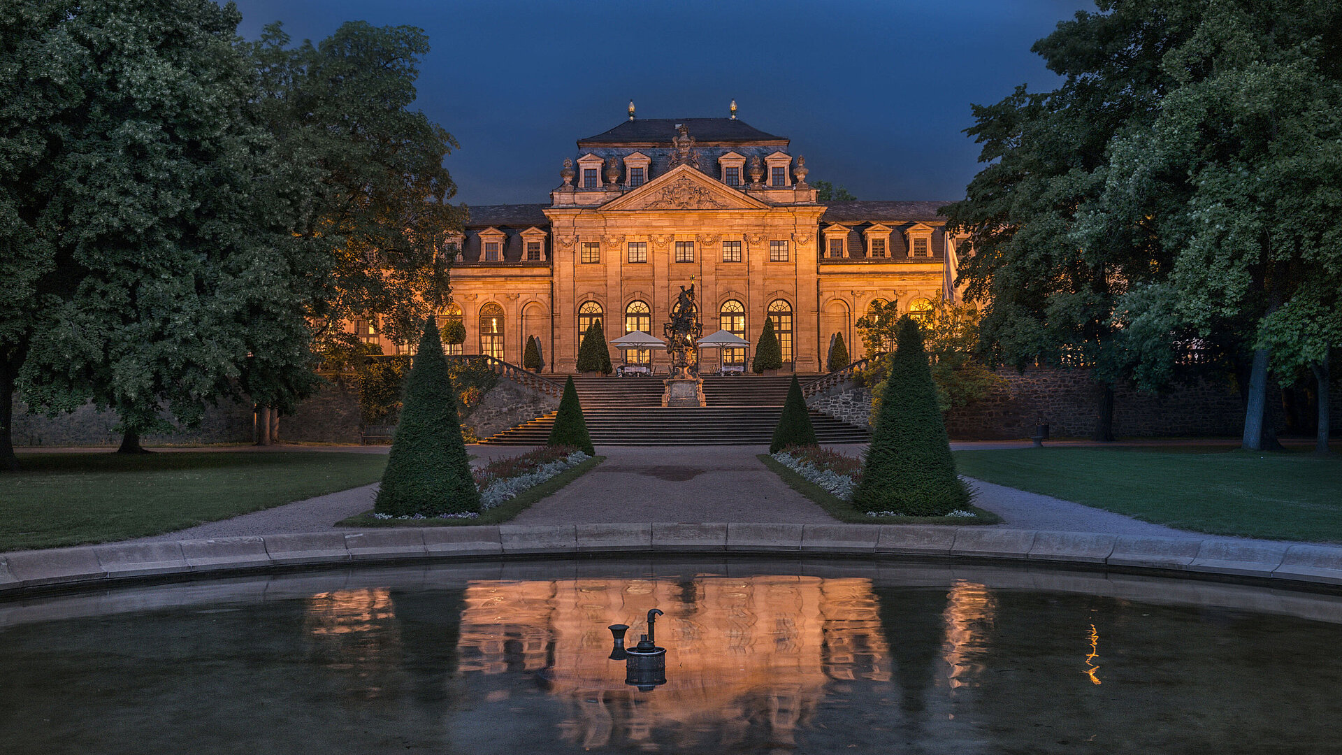 Außenansicht bei Nacht Das Maritim Hotel Fulda, eindrucksvoll beleuchtet bei Nacht, mit Spiegelung im Wasserbecken des Barockgartens.