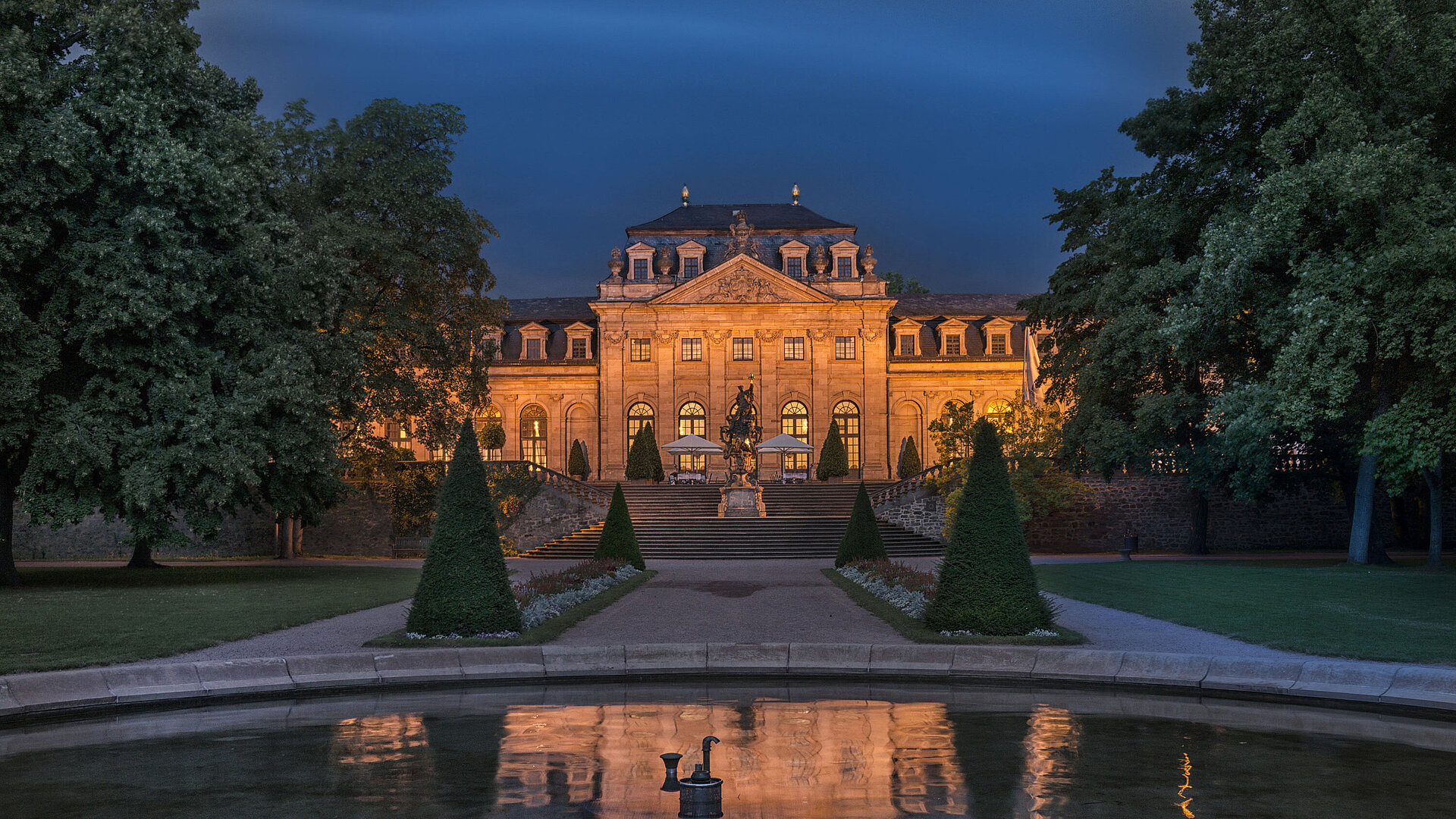 Das Maritim Hotel Fulda, eindrucksvoll beleuchtet bei Nacht, mit Spiegelung im Wasserbecken des Barockgartens.