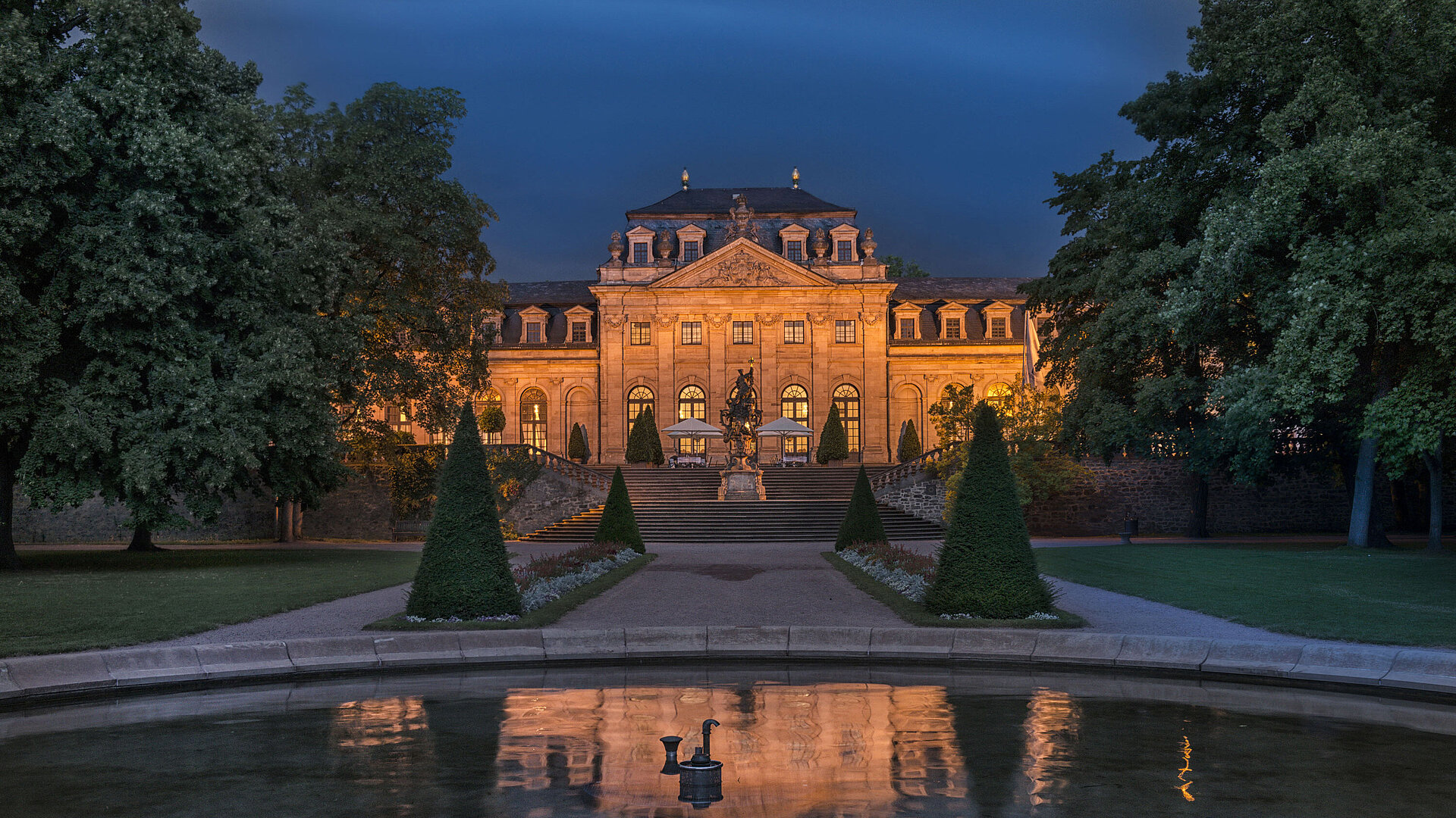 Das Maritim Hotel Fulda, eindrucksvoll beleuchtet bei Nacht, mit Spiegelung im Wasserbecken des Barockgartens.