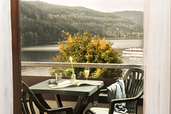 Balkon mit Tisch, Getränk und Blick auf den Titisee und die umliegende Natur
