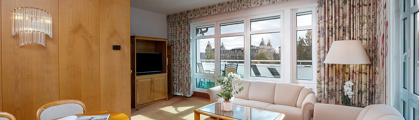 Junior Suite Junior Suite mit hellem Wohnbereich, Sofa, großem Fenster, Essplatz und klassischer Einrichtung im Maritim Hotel.