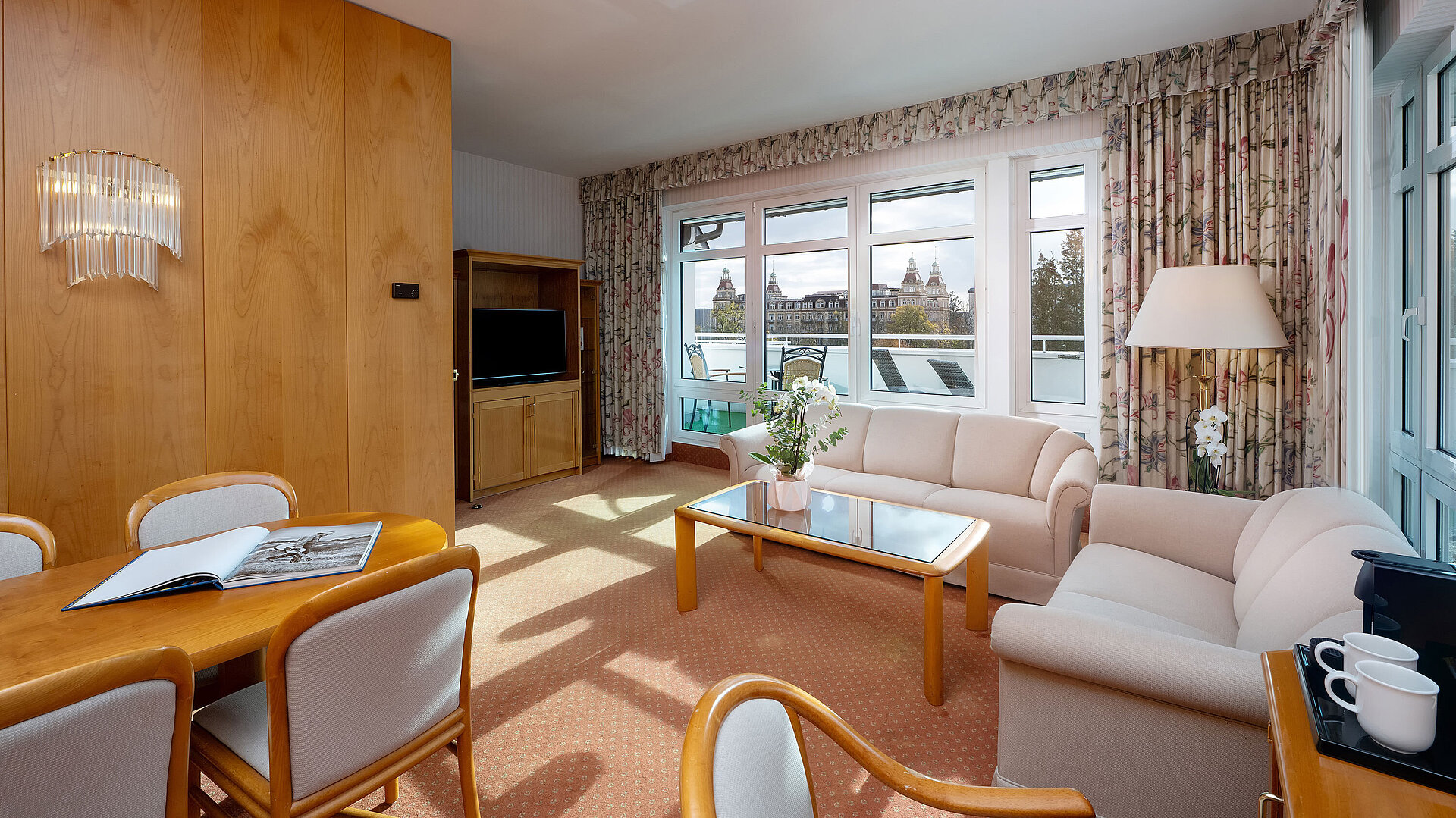 Junior Suite mit hellem Wohnbereich, Sofa, großem Fenster, Essplatz und klassischer Einrichtung im Maritim Hotel.