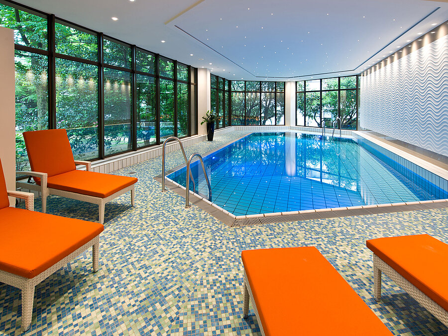 Entspannungsbereich am Pool im Maritim Hotel Bad Homburg mit Blick ins Grüne und orangenen Liegestühlen.