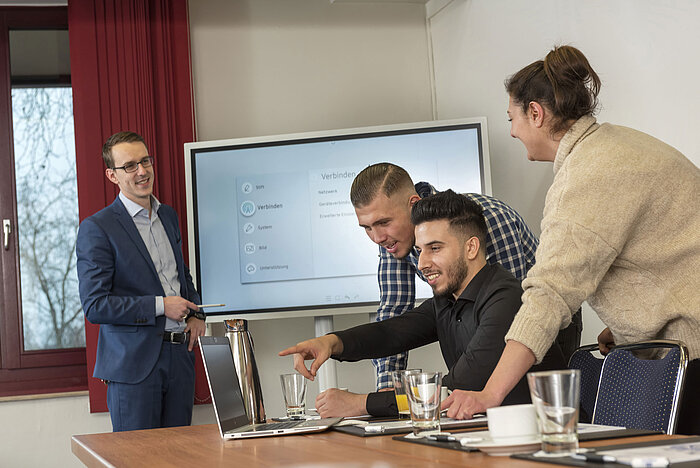Team-Meeting im Salon Rhein im Maritim Köln mit einem Bildschirm, Laptops und Teilnehmern, die zusammenarbeiten.