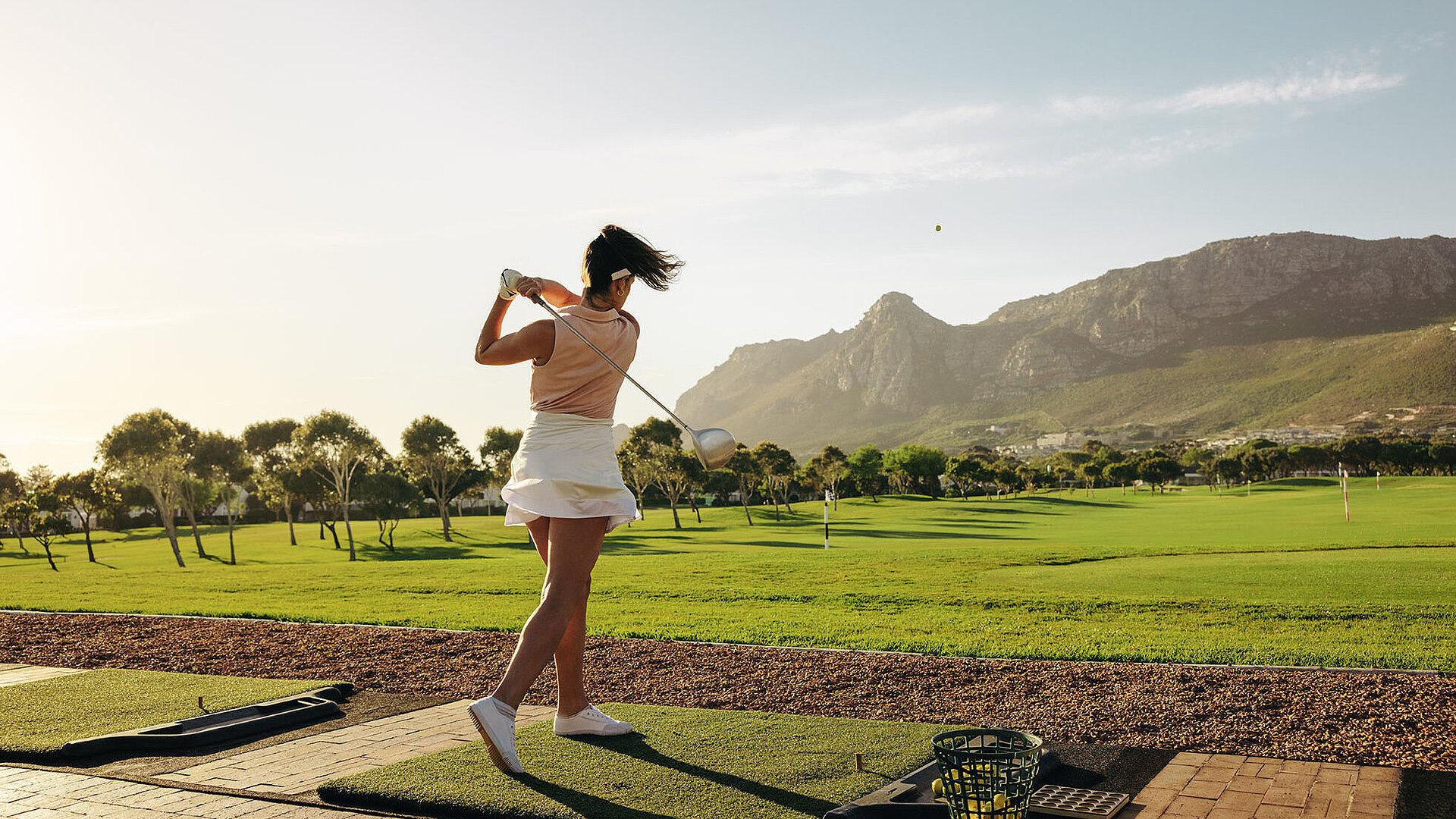 Golferin nach dem Abschlag auf einem Golfplatz mit Blick auf Fairway und Berglandschaft.