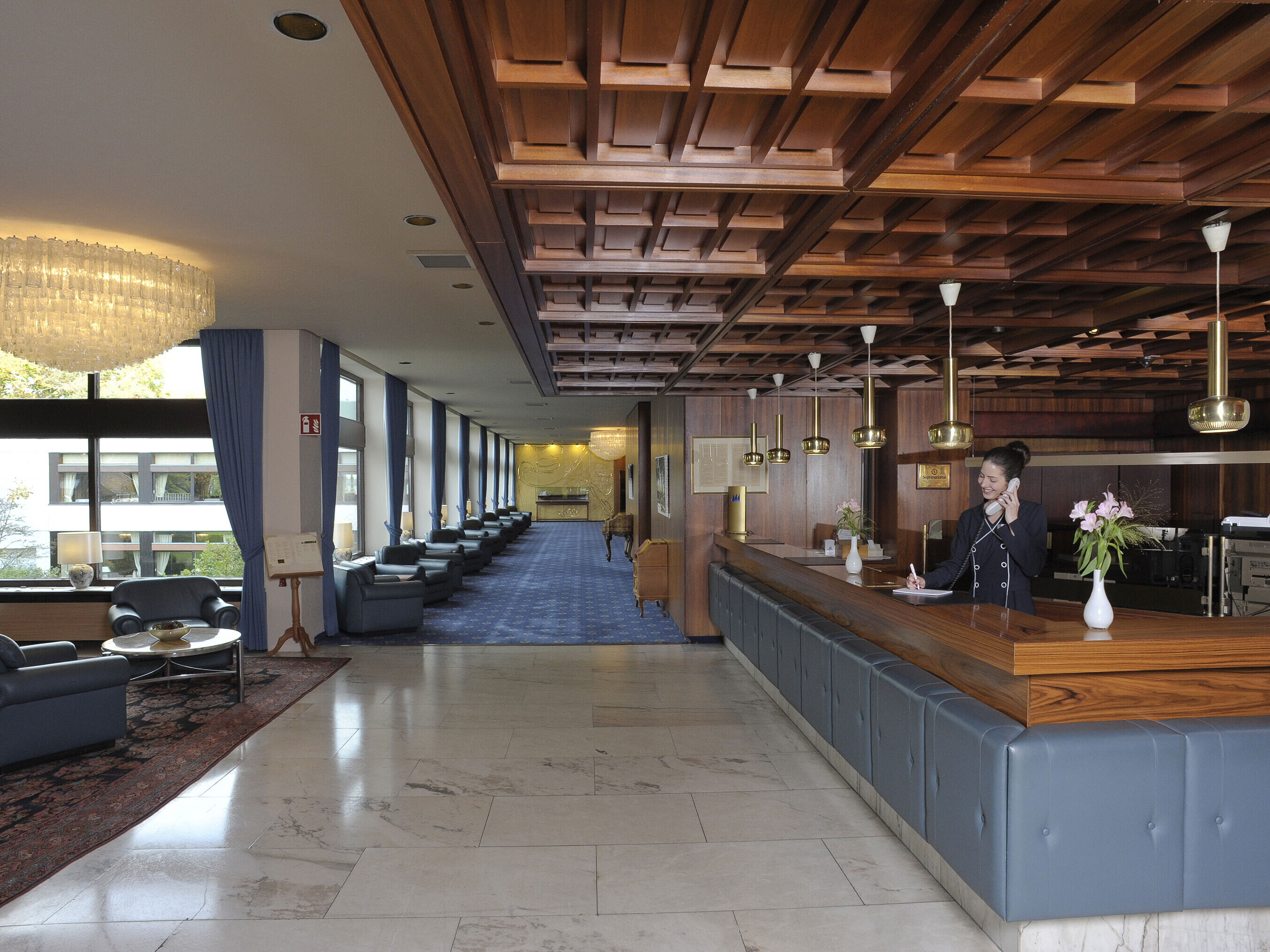 Rezeption im Maritim Hotel Kiel, elegante Holzverkleidung, Kronleuchter und gemütliche Sitzbereiche mit Blick auf große Fenster