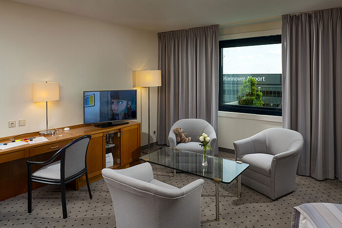 Komfortables Familienzimmer mit Sitzbereich, TV und Ausblick auf den Hannover Airport im Maritim Hotel Hannover.