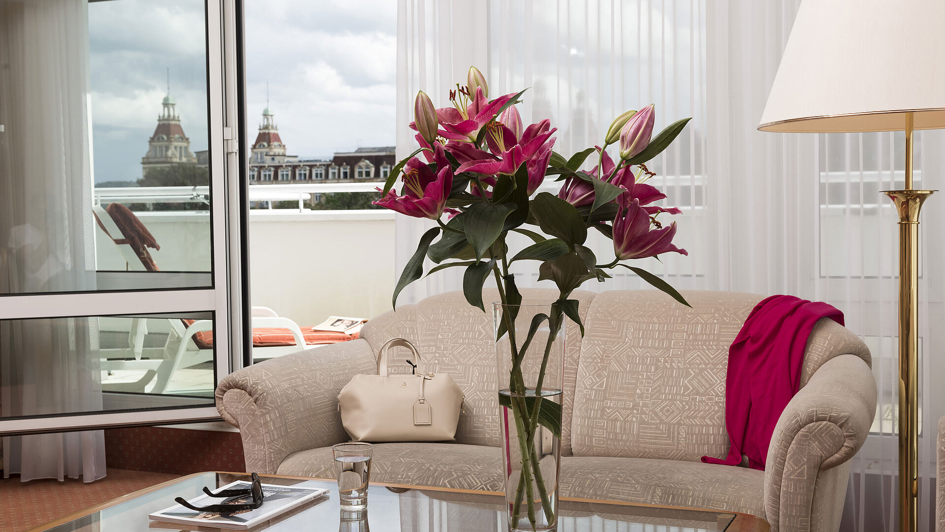 Junior Suite Helles Wohnzimmer mit Blumen, Sofa und Blick auf die historischen Türme vom Balkon im Maritim Hotel Bad Wildungen