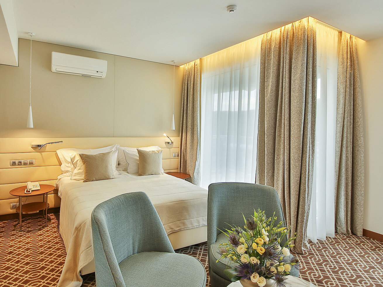 Modernes Hotelzimmer mit Doppelbett, eleganten Möbeln, großen Fenstern und warmem Lichtdesign