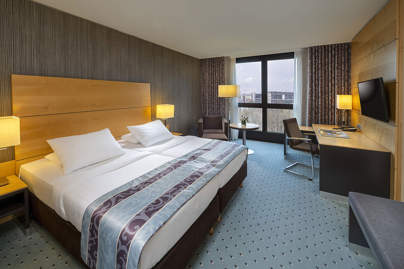 Comfort Zimmer im Maritim Hotel Düsseldorf mit großem Doppelbett, Schreibtisch, Sessel und Panoramafenster.