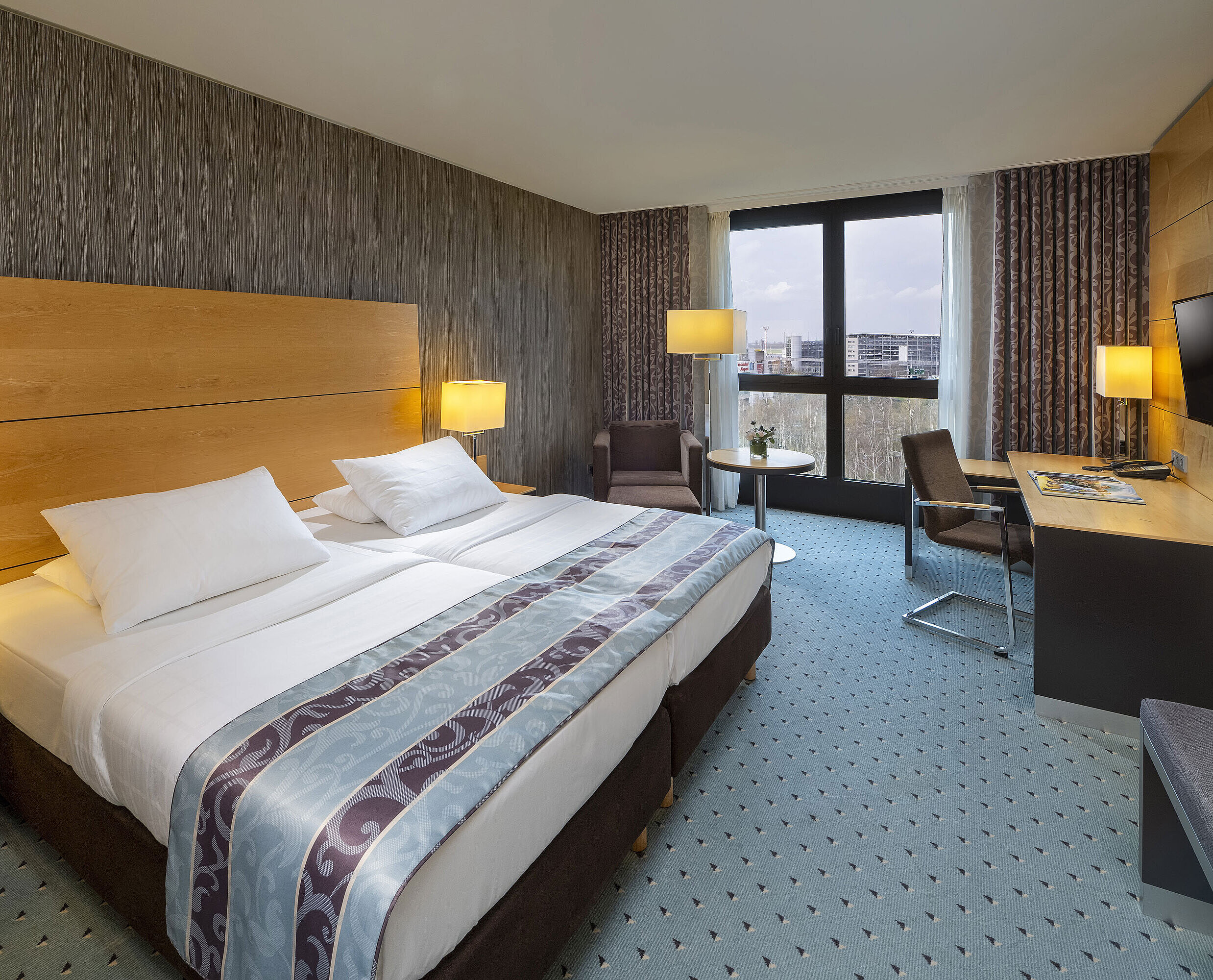 Comfort Zimmer im Maritim Hotel Düsseldorf mit großem Doppelbett, Schreibtisch, Sessel und Panoramafenster.