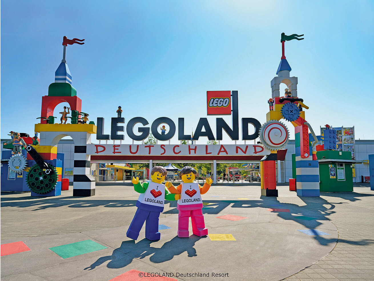 Bunter Eingang des LEGOLAND® Deutschland Resorts mit riesigen LEGO® Figuren und blauem Himmel.