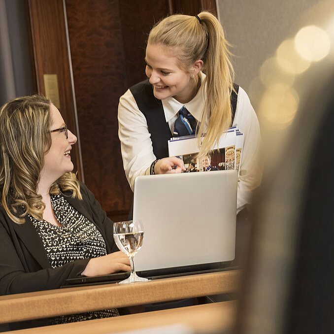 Mitarbeiterin des Maritim Hotel Bonn bietet einer Teilnehmerin während eines Meetings im Salon Rheinaue Unterstützung an.