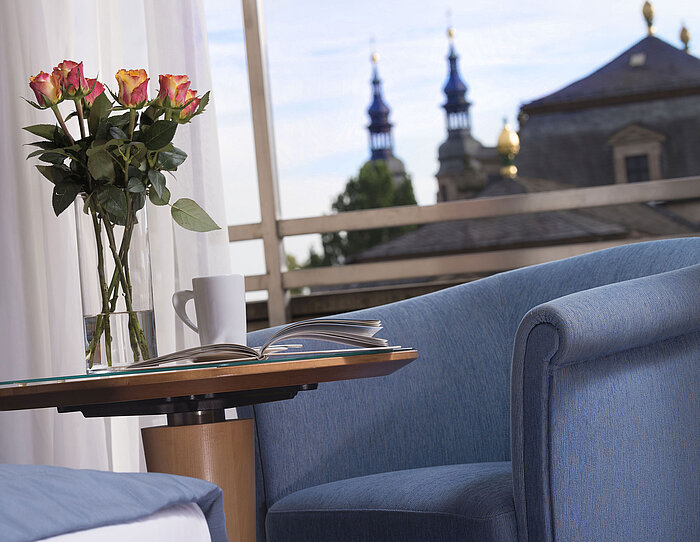 Elegantes Zimmerdetail im Maritim Hotel Fulda mit blauer Sitzgelegenheit, Rosen und Blick auf die barocken Türme von Fulda.