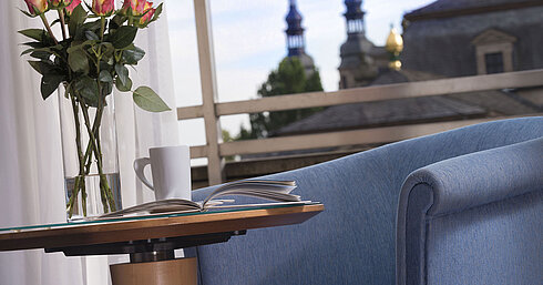 Elegantes Zimmerdetail im Maritim Hotel Fulda mit blauer Sitzgelegenheit, Rosen und Blick auf die barocken Türme von Fulda.