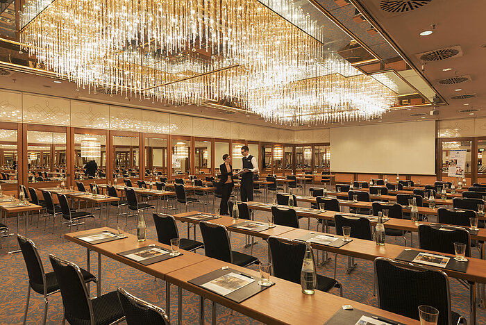 Großzügiger Konferenzsaal mit Kristallleuchtern und gespannter Atmosphäre im Maritim Hotel München
