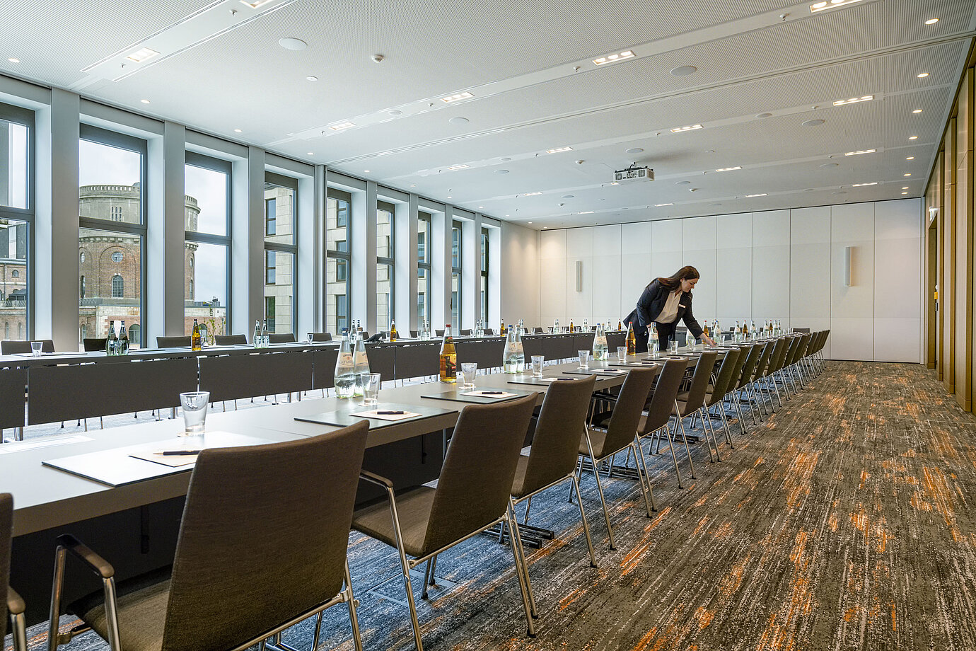 Mitarbeiterin richtet einen modernen Tagungsraum im Maritim Hotel Ingolstadt ein. Große Fenster mit Blick auf die Stadt.