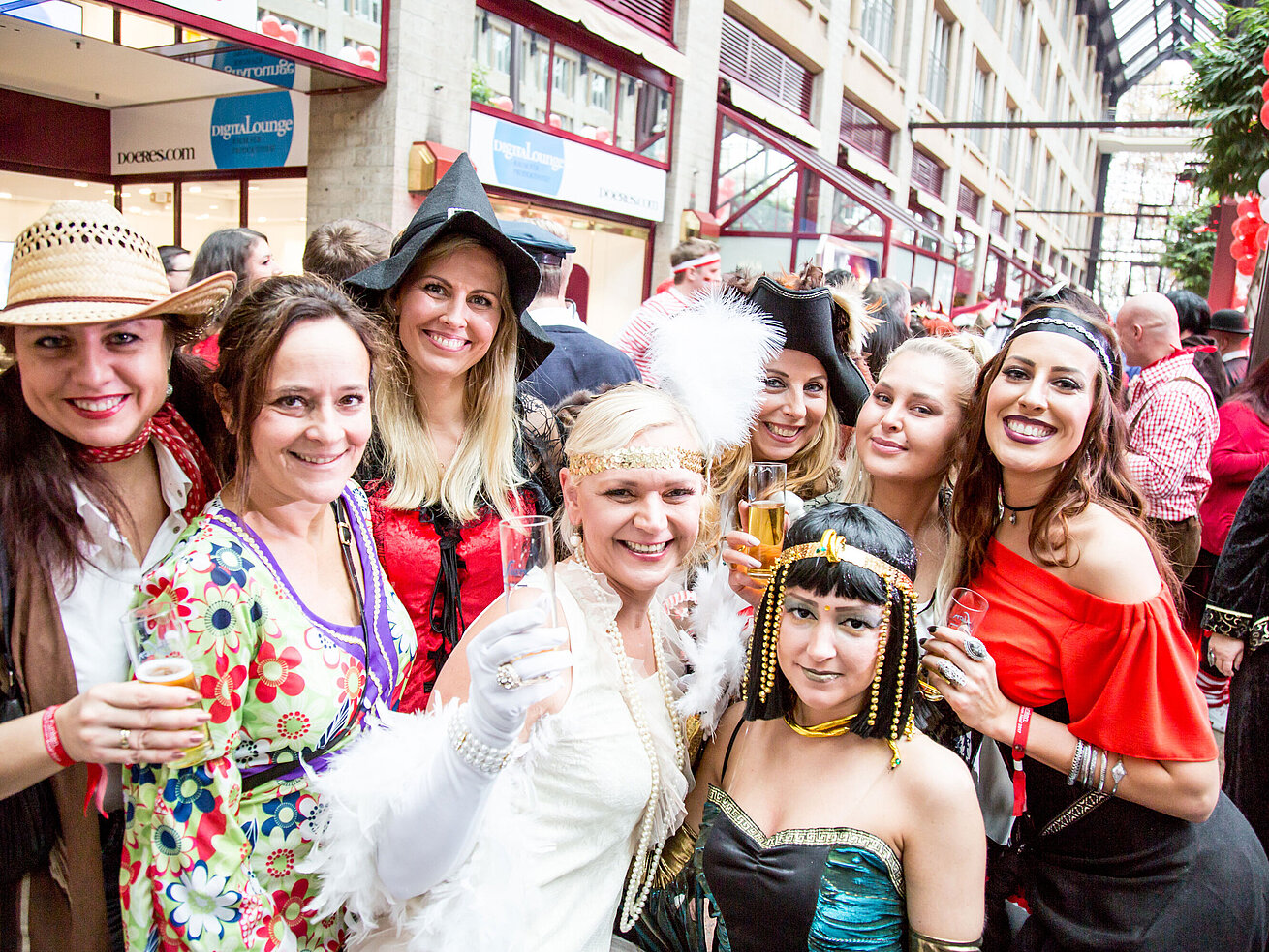 Frauen in bunten Kostümen feiern auf einem Karneval und halten Sektgläser in die Kamera.