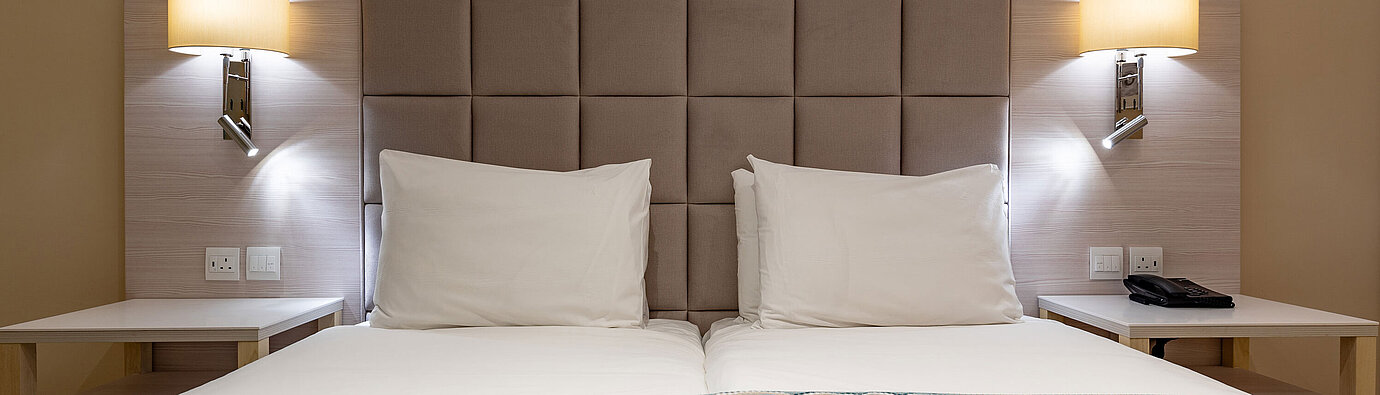 Klassisches Doppelbett mit gepolstertem Kopfteil, Nachttischen und Leselampen im Hotelzimmer