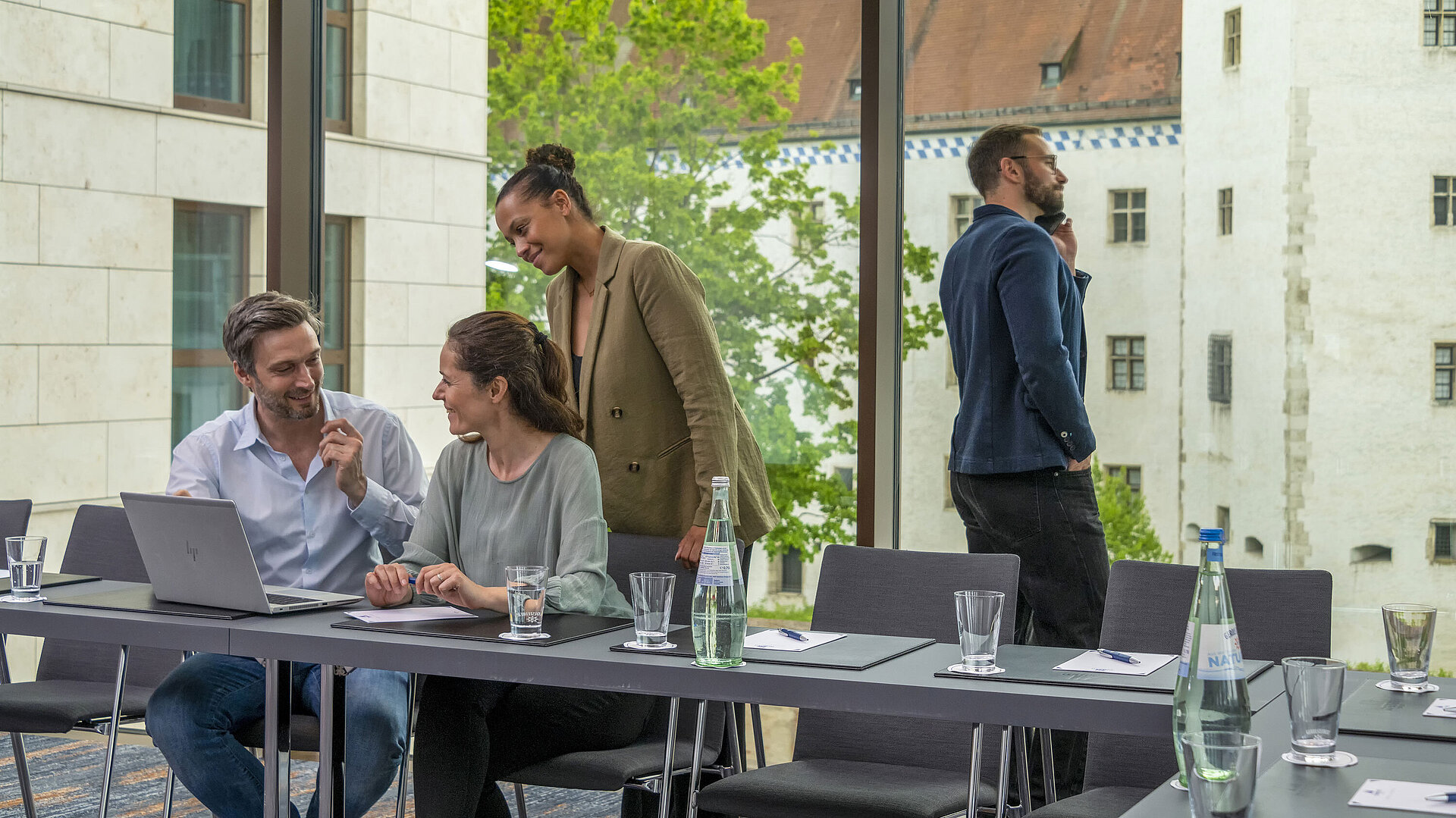 Lächelnde Geschäftsleute im Tagungsraum des Maritim Hotel Ingolstadt mit Blick auf historische Gebäude.