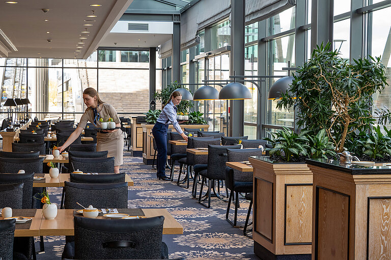 Heller Restaurantbereich Wintergarten im Maritim Hotel Dresden mit großen Fensterfronten und stilvoll gedeckten Tischen.