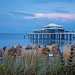 Strandkörbe am Sandstrand mit Blick auf die Ostsee und eine Seebrücke bei Sonnenuntergang.