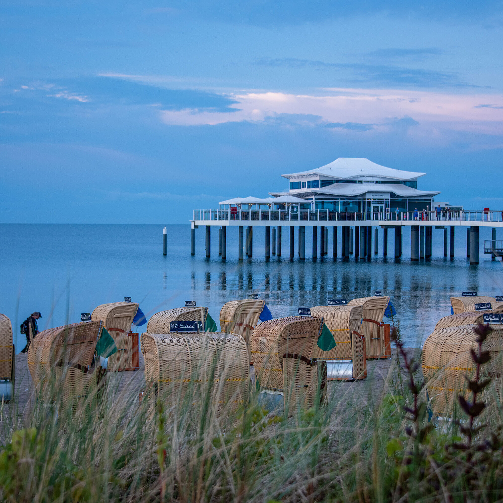 Strandkörbe am Sandstrand mit Blick auf die Ostsee und eine Seebrücke bei Sonnenuntergang.