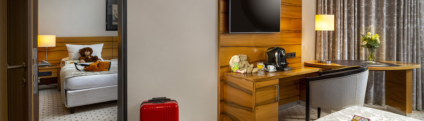 Familienzimmer im Maritim Hotel Bad Homburg mit getrenntem Kinderzimmer, Kuscheltieren und roten Koffer.