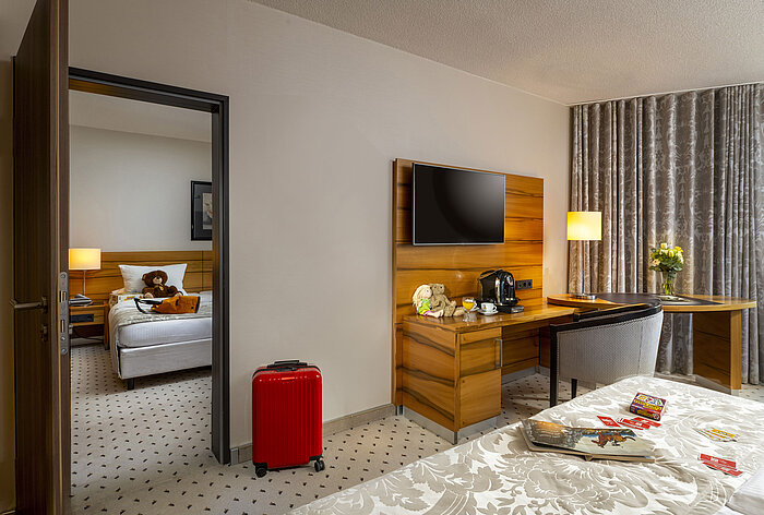 Familienzimmer im Maritim Hotel Bad Homburg mit getrenntem Kinderzimmer, Kuscheltieren und roten Koffer.