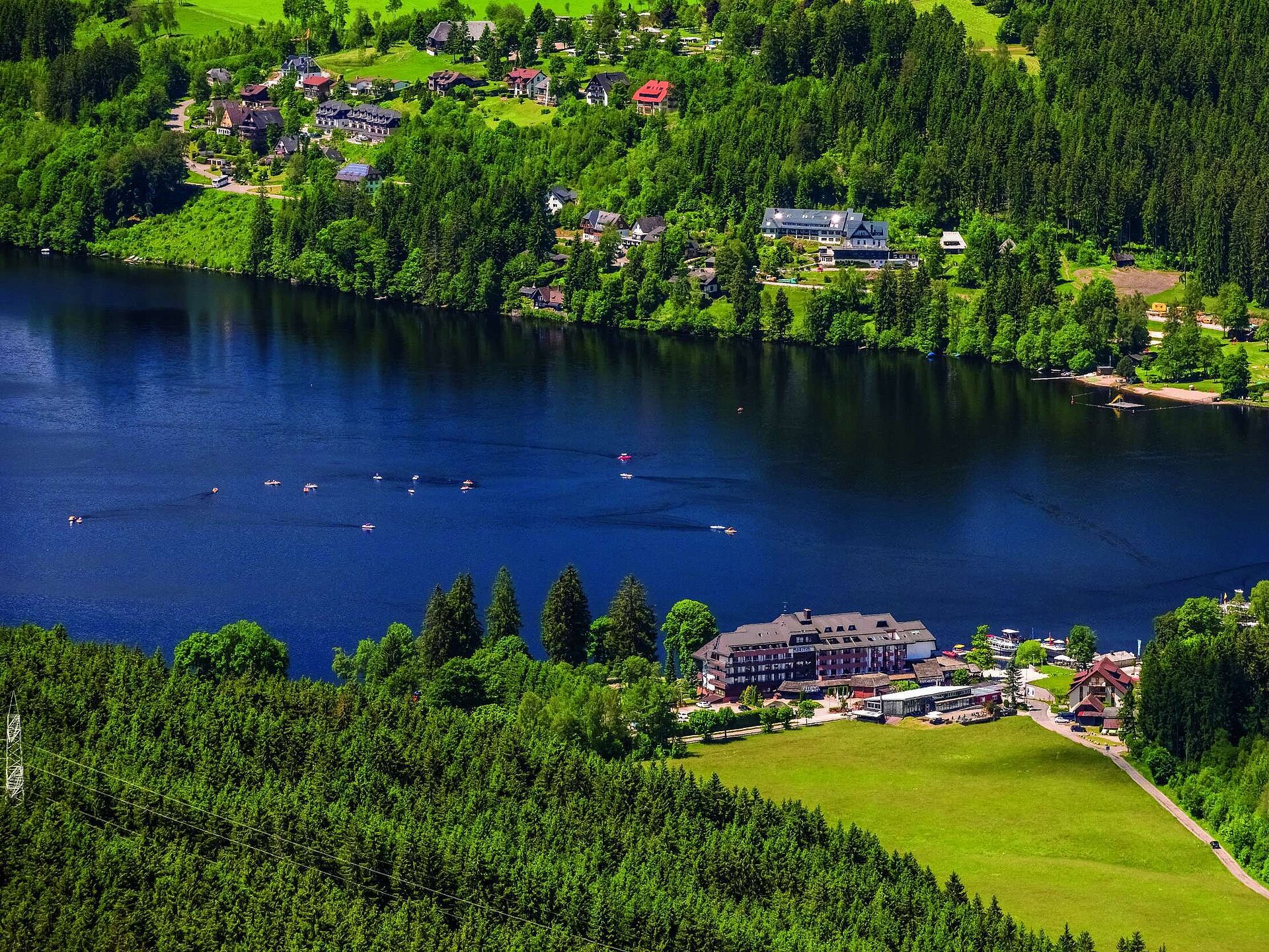 Luftaufnahme des Maritim Hotels direkt am Ufer des Titisees mit umliegendem Wald und Tretbooten auf dem Wasser