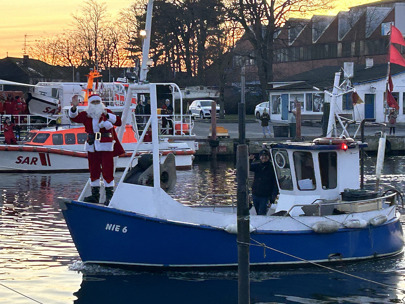 Historisches Fischerboot im Hafen, geschmückt für die Weihnachtszeit, mit winkendem Weihnachtsmann an Bord.
