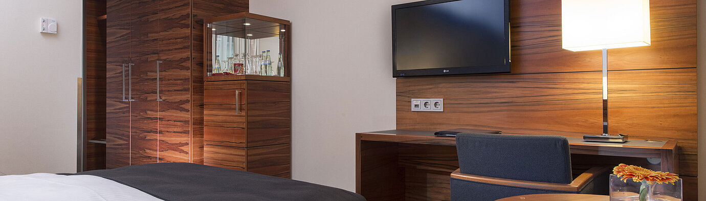 Modernes Zimmer im Maritim Hotel München mit Arbeitsplatz, TV, Sitzgelegenheit und großem Kleiderschrank.