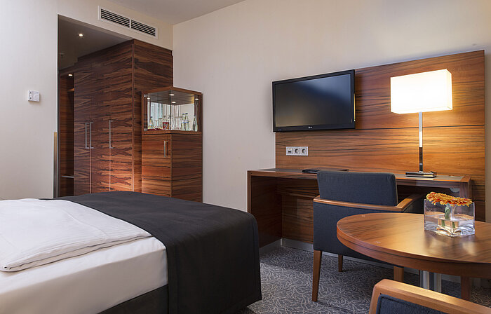 Modernes Zimmer im Maritim Hotel München mit Arbeitsplatz, TV, Sitzgelegenheit und großem Kleiderschrank.