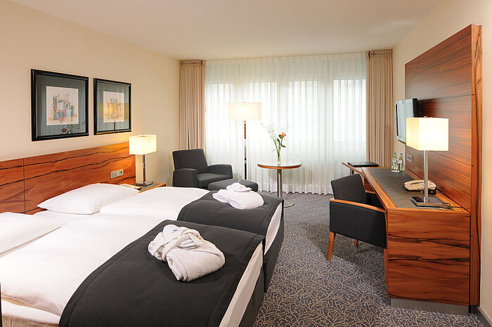 Helles Doppelzimmer mit Schreibtisch, Sesseln und Bademänteln im Maritim Hotel München