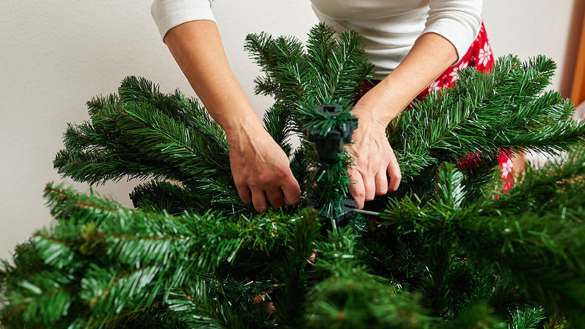 © Jose - AdobeStock.com Hände richten Zweige eines künstlichen Weihnachtsbaums