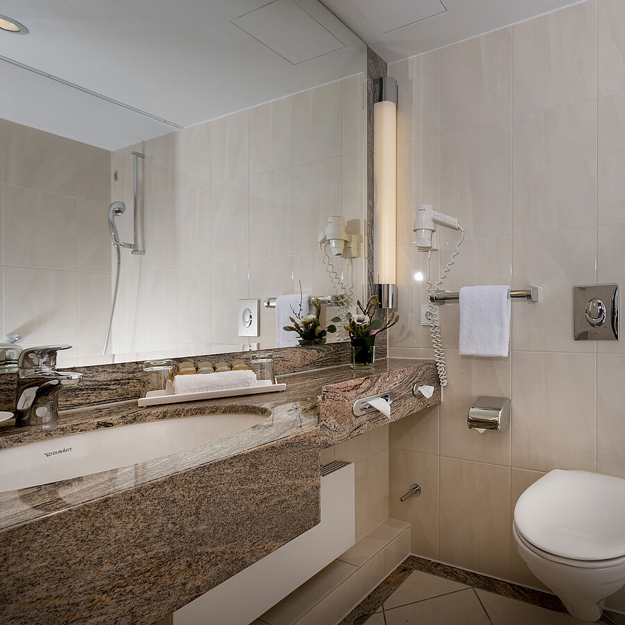 Modernes Badezimmer im Maritim Seehotel Timmendorfer Strand mit Waschtisch, Spiegel, Dusche, WC und Badewanne.