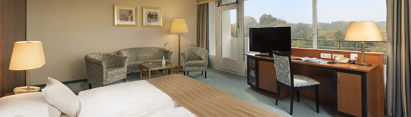 Comfort Zimmer im Maritim Hotel Kiel mit gemütlicher Sitzecke, Schreibtisch, großem Bett und herrlichem Blick ins Grüne.