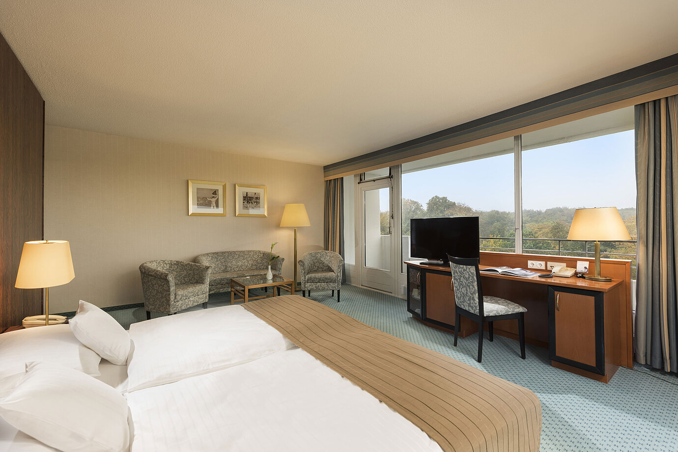 Comfort Zimmer im Maritim Hotel Kiel mit gemütlicher Sitzecke, Schreibtisch, großem Bett und herrlichem Blick ins Grüne.