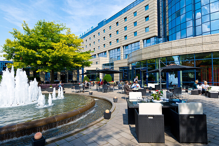 Terrasse des Maritim Hotels Bonn mit Sitzbereichen, Springbrunnen und Gästen, die im Freien speisen und entspannen.