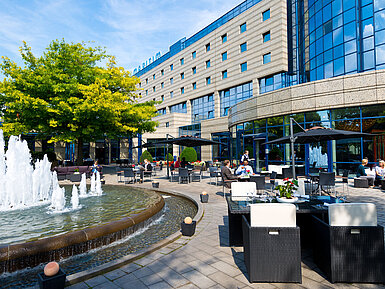 Terrasse des Maritim Hotels Bonn mit Sitzbereichen, Springbrunnen und Gästen, die im Freien speisen und entspannen.