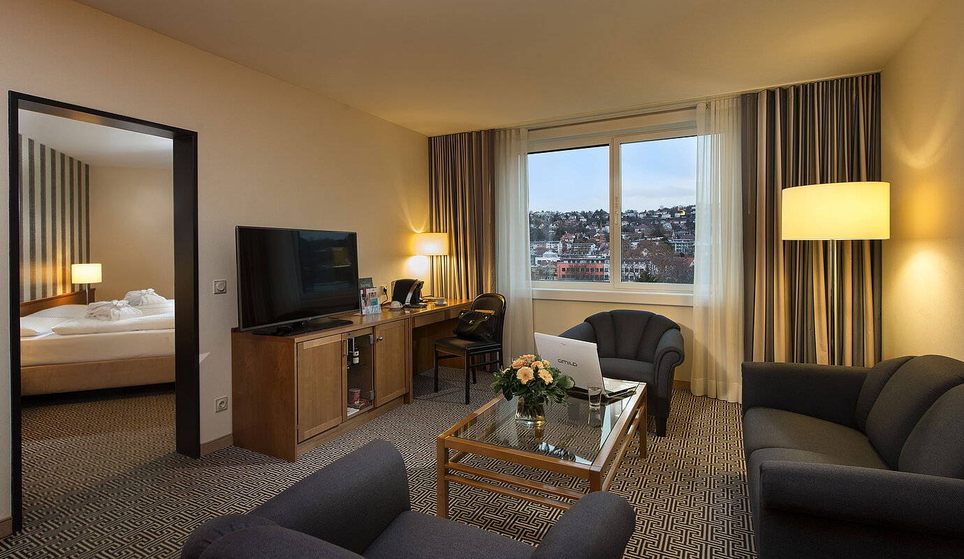 Wohnbereich der Suite mit Sofa, TV, Schreibtisch und Blick auf die Stadt im Maritim Hotel Stuttgart